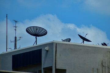 Satellite dishes with tv antenna on top of the old gray building against the sky. Satellite dish with sky on the roof. The satellite dishes, and TV antennas on the roof building in urban.