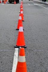 Close-up of the traffic cone on the road. Bright orange traffic cones standing in a row on asphalt. Transportation tool, equipment. Road works. Cityscape.