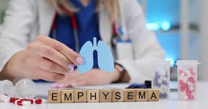 Female doctor holds paper lungs near word Emphysema on wooden cubes. Treatment and prevention of chronic obstructive pulmonary disease at appointment