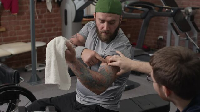 Brutal bodybuilder with disability and his unrecognizable personal trainer checking progress of workout