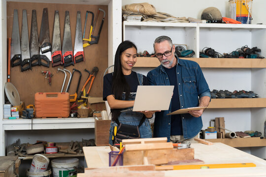 Carpenter, Wood workshop. Two carpenter using laptop computer together in carpenter wood factory - Powered by Adobe