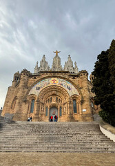 Obraz premium Temple of the Sacred Heart. Tibidabo. Majestic stone church with intricate facade and towering spires, surrounded by lush greenery and steps leading to the entrance, showcasing architectural beauty