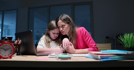 Stressed mother helps young daughter with homework late at night using calculator and laptop. Challenges of working parents and home education - Powered by Adobe