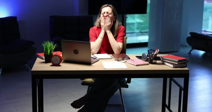 Tired businesswoman works from home at night with chronic fatigue and burnout feeling exhausted. Sleepy lady rubs eyes while sitting at desk in office