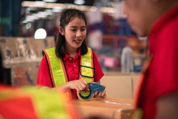 Smiling Factory Worker Packing Boxes for Shipping in Warehouse with Team in Reflective Vests and...