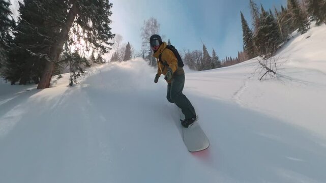 Professional snowboarder riding fast off piste in deep powder forest jumping over snow mounds spraying snow and carving between trees in extreme winter freeride mountain landscape