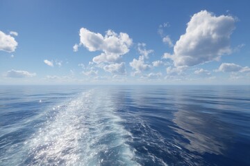 Calm blue ocean with white clouds and boat wake leaving a trail on a sunny day at sea horizon view