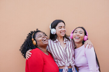 Happy multiracial women having fun listening music playlist with wireless headphones in the city -...