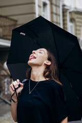 Beautiful girl standing under a black umbrella in the rain