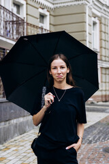 Beautiful girl standing under a black umbrella in the rain