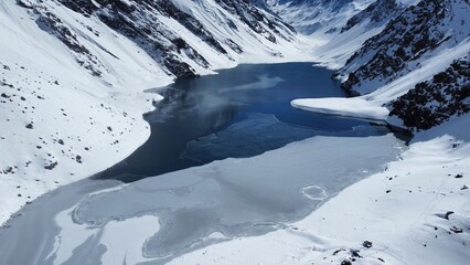 Foto aérea do lago congelado em Portillo, Chile, rodeado por montanhas cobertas de neve. Um espetáculo natural que evidencia a força do inverno nos Andes e o contraste entre gelo e terra © RNL Fotografia