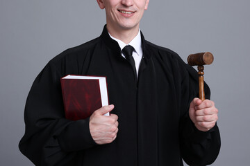 Smiling judge with mallet and book on grey background, closeup