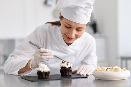 Confectioner decorating cupcake with pieces of chocolate in kitchen