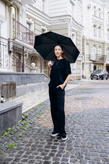 Beautiful girl standing under a black umbrella in the rain