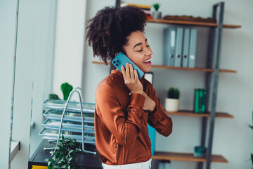 Young businesswoman with natural hair communicating on the phone in a modern office space with shelves and plants