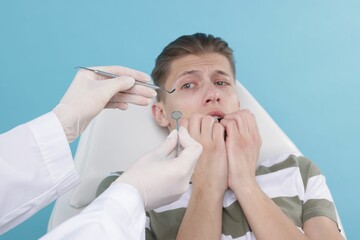 Scared man having appointment with dentist on light blue background