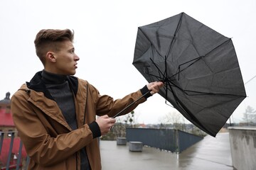 Man with broken umbrella fighting wind under rain outdoors