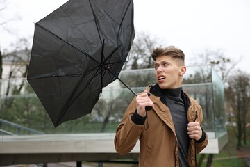 Man with broken umbrella fighting wind under rain outdoors