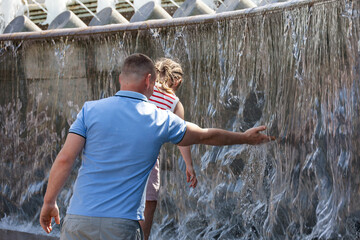 People playing with water jets of fountain. Man and child in summer, hot weather in city