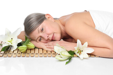 Obraz na płótnie Canvas Senior woman with lily flowers relaxing on bamboo mat against white background