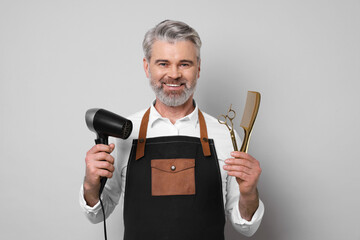 Smiling hairdresser with dryer, scissors and comb on gray background