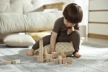 Cute little child playing with wooden building blocks at home