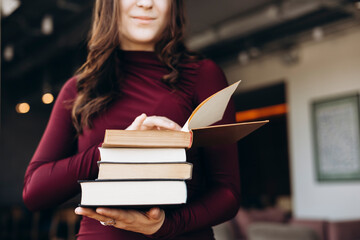 Female student holding stack of books in library