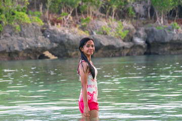 Fototapeta premium Young asian woman in swimsuit standing in tropical river with rocks behind