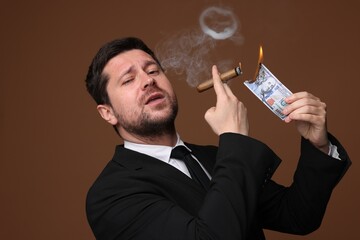Greedy banker lighting cigar with dollar banknote on brown background