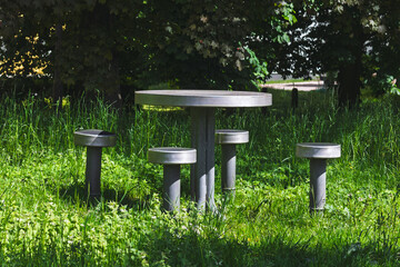 Circular Metal Picnic Table with Four Stools Amid Tall Grass in a Sun-Dappled Park