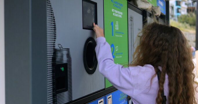 Little girl presses keys choosing options on reverse vending machine display on city street. Reusing waste materials with sustainable technology