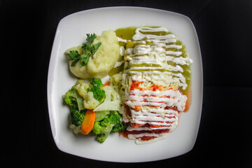 A neatly arranged plate featuring chicken enchiladas in a flavorful sauce, served with mashed potatoes and mixed vegetables, ideal for a fulfilling meal.