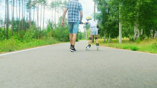 Father and daughter ride on roller skates. Girl learning to roller skate. Dad teaches daughter to ride on rollers