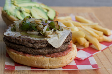 A heaped burger featuring layers of grilled beef, savory toppings, combined with fresh vegetables and surrounded by a handful of crispy fries, perfect for any meal.