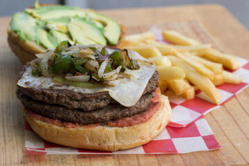 An appetizing burger stacked high with layers of meat, melted cheese, and grilled onions, served with a portion of crispy fries, perfect for satisfying any cravings.