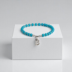 Turquoise gemstone bracelet with 925 sterling silver charm shaped as the letter B, displayed on a white jewelry box, elegant accessory in minimal product shot style