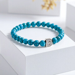 Turquoise gemstone bracelet with 925 sterling silver charm shaped as the letter B, displayed on a white jewelry box, elegant accessory in minimal product shot style