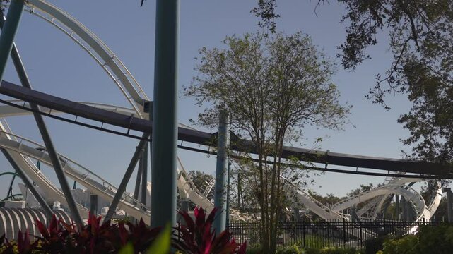 Thrilling moments await as riders scream in joy on a roller coaster at a marine park. The bright sun complements the vibrant greenery and the fun-filled atmosphere.