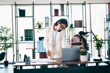 Confident female executive working in a modern office while multitasking with phone and laptop for professional productivity