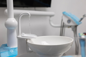 Close-up of a dental clinic sink with water flowing from the faucet beside the dental chair,...