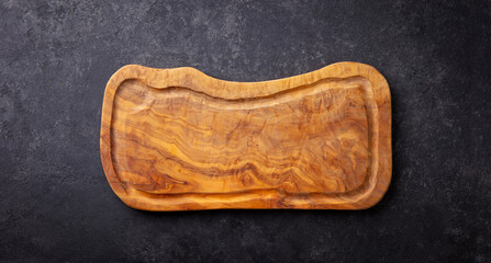 Provencal olive wood chopping board or cutting board. Dark stone background. Copy space. Close up....