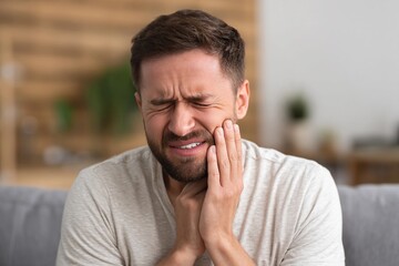Man experiencing dental pain while sitting on couch in a modern living room
