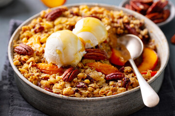 Peach crumble cake with ice cream and pecan nuts in bowl. Grey background. Close up.
