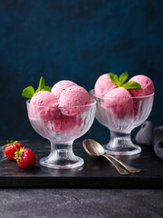 Strawberry ice cream in a glass bowl on marble cutting board. Dark background. Close up. Copy space.