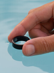 Hand, submerged in pool water showcasing a sleek waterproof black smart ring with health tracker.
