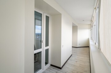 bright, narrow balcony with white walls, many windows, and wood-patterned floor. Natural light fills the space.