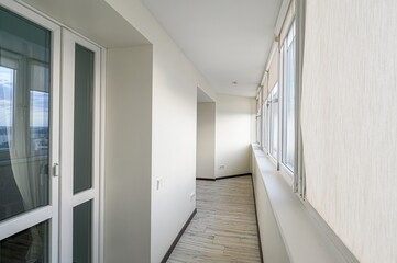 Obraz premium bright, narrow balcony with white walls, many windows, and wood-patterned floor. Natural light fills the space.