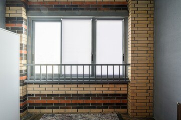 Interior view featuring a window with blinds, set within brickwork. A metal railing is placed in...