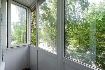 Bright balcony with white frames and large windows overlooking lush green trees, bringing the...