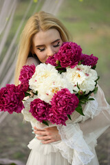 photo shoot for a girl in a white dress with a bouquet of peonies in bed in nature